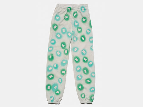 100% cotton light grey/cement sweatpants, perfectly cut, with hand-painted, green and teal, negative cut-out squares extending across body and down legs. The pattern continues on the other side of the pants. 